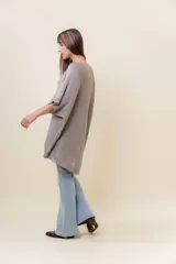 Maxi sweater tejido color beige con efecto metalizado sutil, silueta amplia, mangas tipo murciélago y largo asimétrico (más corto adelante y más largo atrás).