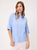 Camisa de manga corta celeste, confeccionada en mezcla de algodón y lino, con cuello camisero y cierre frontal de botones.