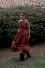 Vestido largo color marrón de crepé plissé, con escote halter adornado con detalles de perlas, silueta fluida y lazo ajustable en la cintura.
