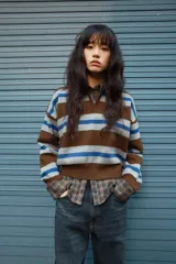 Jersey de punto con diseño a rayas horizontales en tonos marrón, gris y azul. Presenta cuello tipo polo con abertura frontal, manga larga y puños acanalados.
