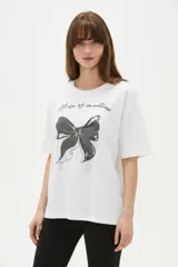 Remera blanca de algodón de manga corta, con cuello redondo y corte holgado. Presenta estampado frontal de un lazo con detalles de brillos y la frase 'Made of sweetness'.
