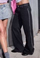 Jean de corte recto y tiro bajo, color negro, con detalle de tachas metálicas en la cintura y una banda lateral de brillos a lo largo de la pierna.