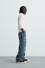 Jeans de corte relaxed fit en denim de algodón, color azul medio lavado. Presenta bordados florales en color blanco o crudo distribuidos en las piernas. Modelo de cinco bolsillos con cierre frontal de cremallera y botón.