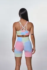 Conjunto deportivo compuesto por un top de escote redondo con breteles finos y un short ciclista de tiro alto. Ambas piezas presentan un diseño estampado estilo tie-dye en tonos pastel de azul, rosa y verde, con el logo de la marca estampado en el frente del top.