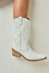 Bota texana blanca de caña media realizada en cuero engrasado, con detalle de punta fina y bordado decorativo. El interior está forrado en cuero vacuno. El taco es de madera.