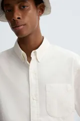 Camisa de algodón color blanco hueso, de corte regular, con cuello abotonado, manga larga terminada en puño con botón y bolsillo de parche en el pecho.