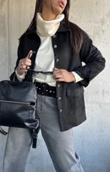Chaqueta de gamuza negra con cierre frontal de botones metálicos, bolsillos laterales y cuello camisero.