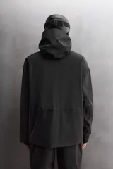 Cazadora deportiva de esquí en color negro, confeccionada en tejido técnico impermeable de tres capas con costuras y cremalleras termoselladas. Cuenta con capucha ajustable, ventilación en axilas, puños con ajuste de tira adherente y puño interior elástico con abertura para el pulgar. Incluye sistema de rescate RECCO y faldón interior para protección contra el frío.