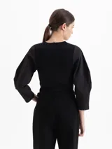 Top de tejido de punto acanalado en color blanco, con cuello redondo y mangas tres cuartos de tela plana con volumen. Presenta un diseño ajustado al cuerpo que contrasta con la estructura de las mangas.