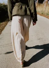 Pantalón balloon de tiro medio en color beige con estampado de rayas finas verticales oscuras. Presenta diseño abombado con bajo ajustable mediante botón.