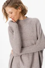 Sweater de punto color marrón chocolate, de corte holgado y diseño oversize. Presenta cuello alto tejido, mangas largas con puños acanalados extendidos hasta el codo y ruedo acanalado.