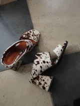 Sandalias de tacón alto y ancho, confeccionadas en piel con acabado de pelo y estampado animal print de vaca en tonos marrones y blancos, con tiras anchas en el empeine.