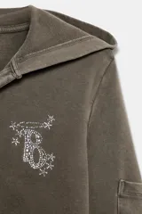 Sudadera de algodón color gris oscuro con capucha, manga larga y detalle de texto con aplicación de brillos en el pecho. Presenta un diseño con bolsillos laterales en las mangas y bajo recto.