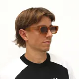 Lentes de sol con armazón de acetato en tono ámbar traslúcido y cristales degradados. Presentan un diseño de marco cuadrado con patillas gruesas y detalle metálico en la unión.