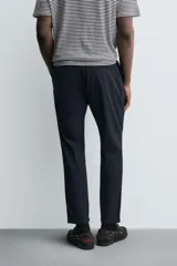 Pantalón de corte slim fit y color negro, confeccionado en tejido elástico. Cuenta con cintura elástica, trabillas, bolsillos frontales y cierre con cremallera y botón.