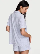 Pijama corto de Victoria's Secret confeccionado en suave mezcla de modal, de color celeste con estampado de monogramas. Incluye una camisa de manga corta con solapas, cierre frontal de botones y un bolsillo en el pecho, acompañada de un short con cintura elástica.