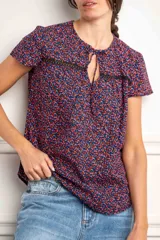 Blusa azul con estampado floral en tonos rosa y celeste, con mangas cortas, cuello redondo con abertura en forma de lágrima y detalle de encaje negro en el pecho.