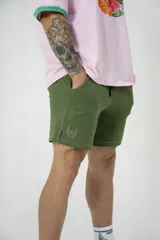 Short deportivo de lycra verde con cintura elástica ajustable con cordón, bolsillos laterales y logo bordado en color rosa.
