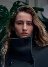 Abrigo de paño en color gris oscuro, con cuello alto, cierre frontal cruzado y cinturón ajustable a la cintura. Presenta mangas largas con detalle de trabillas en los puños.