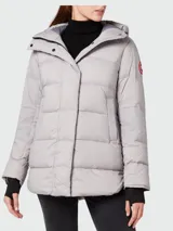 Campera puffer gris claro con capucha, cierre frontal con botones a presión y logo de Canada Goose en el brazo izquierdo.