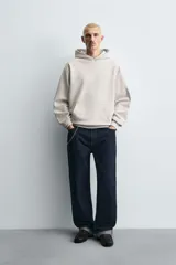 Sudadera tipo hoodie de color blanco hueso, con capucha, manga larga y bolsillo canguro frontal. Presenta un calce relajado y tejido de algodón con interior afelpado.