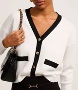 Cardigan de punto blanco con escote en V, botones metalizados, bolsillos falsos, cuello y vista contrastantes en negro, y bajo acanalado.