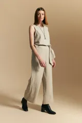 Pantalón de vestir de tiro alto, color beige claro con finas rayas verticales oscuras. Es de corte ancho y largo, con un lazo de tela a juego anudado en la cintura. Se combina con un top sin mangas del mismo tejido y color.