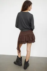 Falda pantalón de tiro bajo en color negro, con cintura drapeada y detalle de tira lateral colgante. Presenta un diseño con volantes en el bajo y cierre de cremallera metálica.