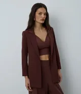 Blazer de sastrería color marrón, modelo oversized de corte alargado. Confeccionado en crepé, presenta solapas clásicas, bolsillos frontales y detalle de pliegues en los puños.