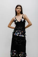 Vestido largo negro con escote en V y tirantes finos. Presenta un diseño de paneles horizontales que alternan bandas de lentejuelas negras brillantes con bandas decoradas con aplicaciones de lentejuelas iridiscentes en forma de pétalos.