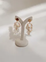 Caravanas colgantes con diseño de pétalos superpuestos en color blanco nacarado y bordes dorados, con base circular dorada.
