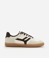 Championes de estilo urbano con diseño retro, confeccionados en material sintético color crema con detalles en marrón oscuro. Presentan recortes laterales, cierre con cordones y suela de goma color caramelo.
