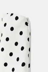 Top palabra de honor de color blanco con estampado de lunares negros, diseño sin tirantes y bajo con volados tipo peplum.