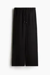 Pantalón negro de piernas amplias con bolsillos laterales discretos. Tiene elástico revestido en la cintura y un cordón para ajustar con cuentas doradas decorativas en los extremos.