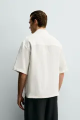 Camisa tipo kimono de corte relaxed fit, color celeste, confeccionada en tejido fluido de viscosa y lino. Presenta cuello con solapas de muesca, manga corta y cierre frontal cruzado con doble botonadura.