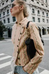 Cazadora de jacquard con estampado de rayas y detalles florales en tonos rosados y beige, cuello redondo, manga larga, bolsillos delanteros de vivo y cierre frontal cruzado con botones metálicos.