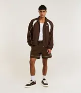 Bermuda deportiva masculina color marrón, con cintura elástica y cordón ajustable. Presenta piping contrastante en blanco a lo largo de los bordes y bolsillos funcionales. Confeccionada en poliamida de secado rápido.