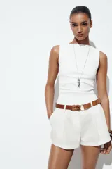 Bermuda blanca de tiro alto con pliegues frontales y bajo ancho. Incluye un cinturón trenzado de cuero marrón con hebilla redonda metálica.