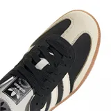 Championes Adidas modelo Samba OG, con diseño clásico de perfil bajo. Presentan una base de gamuza negra con las icónicas tres tiras laterales y puntera en tono crema, finalizando con una suela de goma color caramelo.