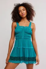 Vestido corto turquesa estilo slip, confeccionado en tela liviana con fruncidos en el cuerpo. Presenta escote recto, tirantes con detalles de encaje, cierre delantero con ganchos y una falda con volados terminada con un aplique de encaje en el borde inferior.