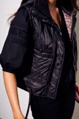Chaleco negro con cierre frontal y cuello alto, de corte al cuerpo y diseño acolchado. Reversible, con interior a cuadros.