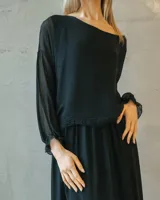 Vestido midi negro de seda italiana, con diseño de capas superpuestas, mangas largas translúcidas y silueta fluida.