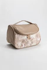Necessaire de viaje con diseño combinado en color beige, presentando una parte superior lisa en cuero sintético y una parte inferior con estampa floral en tonos tierra. Cuenta con cierre superior con doble tirador metálico y manija superior para transporte.