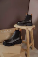 Botas tipo chelsea de cuero negro con textura granulada, paneles laterales elásticos y suela track robusta de goma.