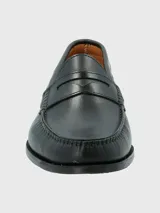 Zapato tipo mocasín de cuero negro con diseño clásico, costuras visibles en la puntera y detalle de antifaz en el empeine.