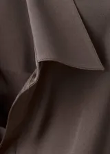 Camisa de tejido satinado color marrón, con cuello camisero cruzado, diseño recto y cierre de lazo cruzado en el lateral. Cuenta con mangas largas y puños anchos abotonados.