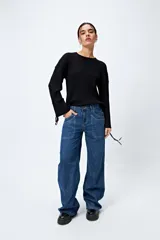 Sweater color crema de tejido de canalé con detalle de trenzado en las mangas y terminación con lazo ajustable.