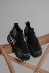 Botas tipo chelsea de caña baja, confeccionadas en una combinación de cuero gamuzado y cuero texturizado en tono marrón oscuro. Presentan una suela track de plataforma gruesa y elásticos laterales negros.