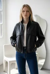 Campera tipo bomber de ecocuero negro con cierre frontal, cuello alto y puños elásticos. Presenta un diseño con costuras horizontales en el pecho y bolsillos laterales con cierre.