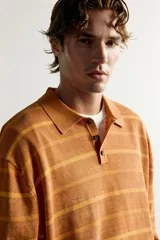 Polo de punto de algodón con diseño a rayas horizontales en tonos tostado y amarillo, cuello solapa y cierre frontal parcial con tres botones. Presenta mangas largas y efecto lavado.